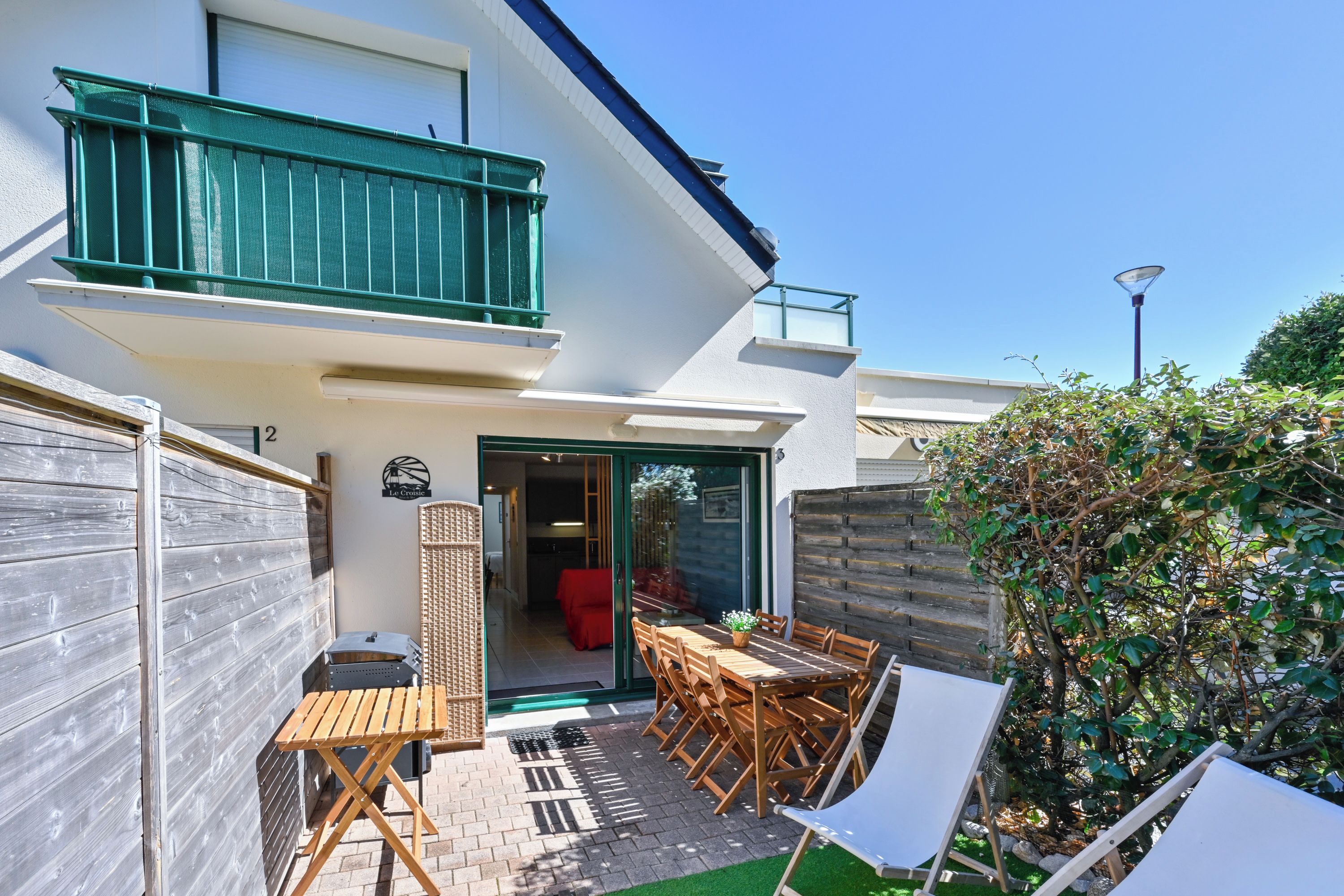 A residential property with a balcony, a patio with a table and chairs, and a small garden area.