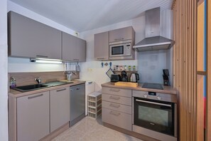 A modern kitchen with grey cabinets, a built-in dishwasher, a microwave, a stove, and a coffee maker. - Brise de Mer - Plage - Terrasse (Le Croisic)