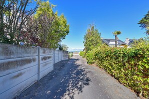 A narrow road flanked by a concrete wall and dense foliage, leading to a residential area with houses and a clear sky. - Brise de Mer - Plage - Terrasse (Le Croisic)