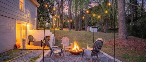 A backyard with a fire pit, outdoor seating, and string lights.
