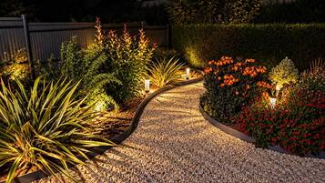 Een grindpad in een tuin, omringd door diverse planten en verlicht met sfeerverlichting.