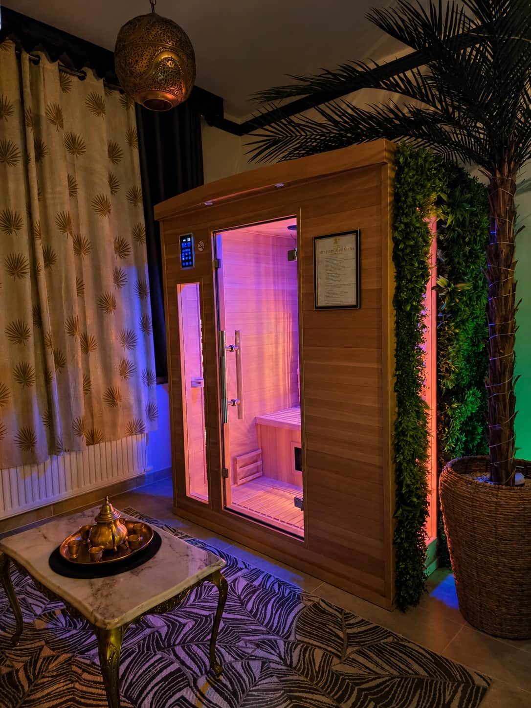 A sauna room with a wooden door, a small table with a tray, and a potted plant.