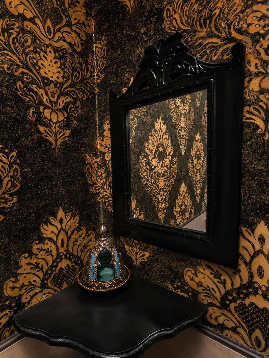 A black-framed mirror with a gold damask pattern on a wall.