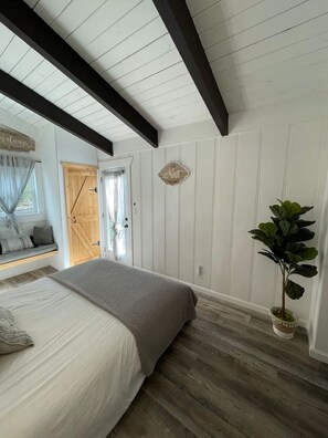 Un dormitorio con una cama, una planta en maceta, una puerta de madera y un letrero en la pared.