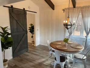 Een eetruimte met een houten tafel, witte stoelen, een kroonluchter en een schuifdeur in boerderijstijl.