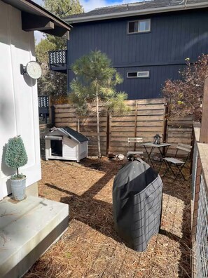 Ein Garten mit Holzzaun, Hundehütte, Terrassentisch und Grill.