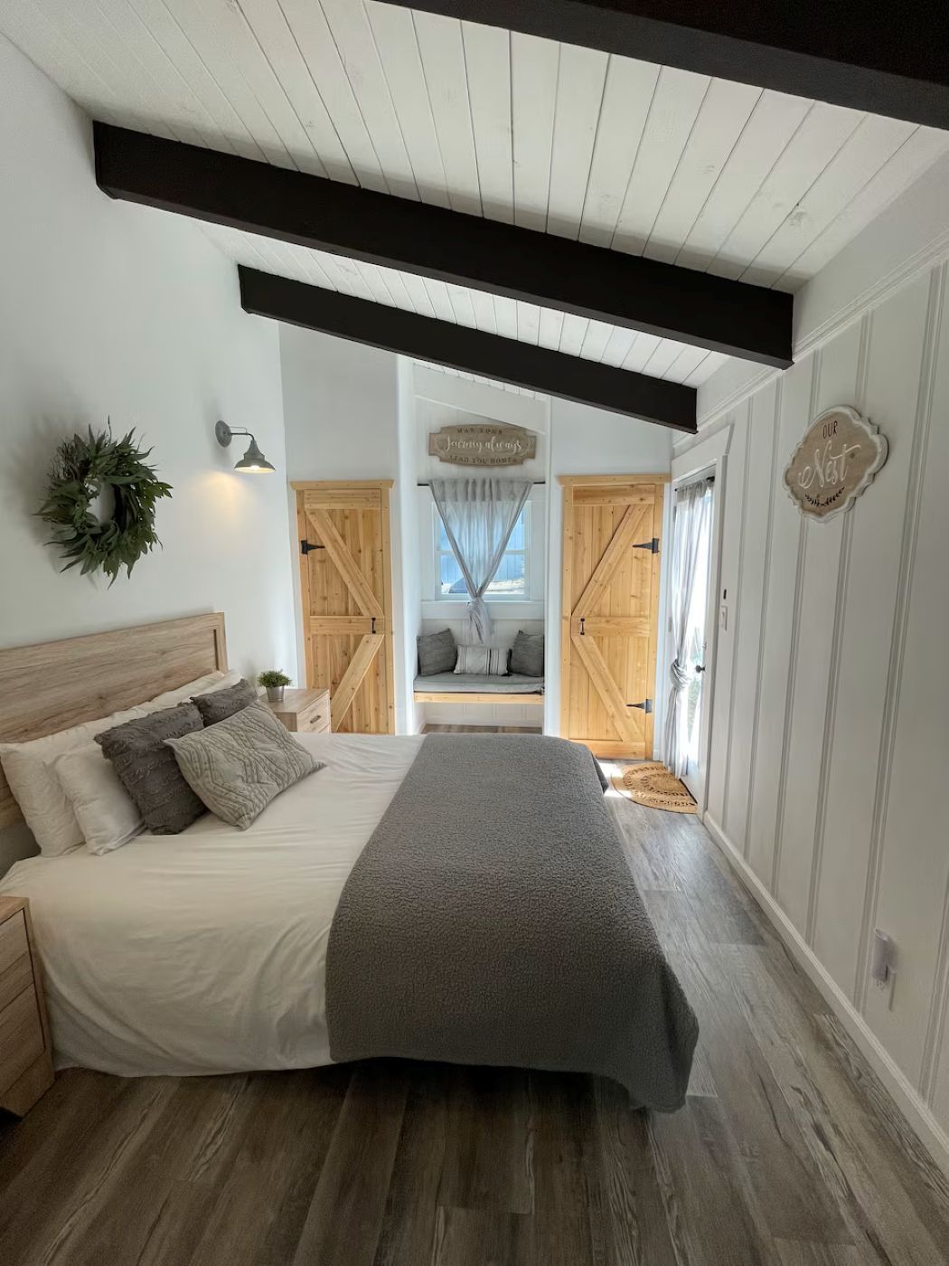 A bedroom with a bed, a headboard, a wall-mounted light, a decorative wreath, and a sign.