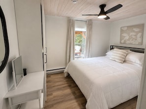 A bedroom with a bed, a ceiling fan, a window with curtains, and a view of the outdoors. - Cozy Lakefront Cottage with Fireplace | ATV & Snowmobile Getaway near Bancroft | Sleeps 6 (Faraday)