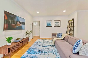 A living room with a large flat-screen TV, a sofa, a coffee table, a patterned rug, and a bookshelf. - PB Hot tub Large Guesthouse + MiniGolf Sleeps 16+ (San Diego)