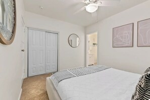A bedroom with a bed, a ceiling fan, a door, and two framed abstract artworks. - PB Hot tub Large Guesthouse + MiniGolf Sleeps 16+ (San Diego)