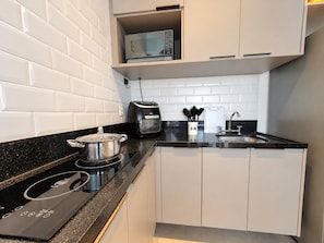 Een moderne keuken met witte kasten, een zwart aanrecht, een magnetron, een broodrooster en een pan op een inductiekookplaat.