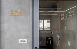 Een moderne, minimalistische vergaderruimte met een glazen scheidingswand, een zichtbaar buitenbalkon en een telefoon aan de muur.