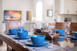 A dining table set with blue bowls and wine glasses, a wooden bowl with pinecones, and a painting on the wall. - The Triple Naples Collection - 3 Homes • Pools & Spas • King Beds! (Naples)