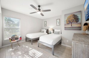 A bedroom with two beds, a ceiling fan, a window with blinds, a chair, and a painting on the wall. - The Triple Naples Collection - 3 Homes • Pools & Spas • King Beds! (Naples)