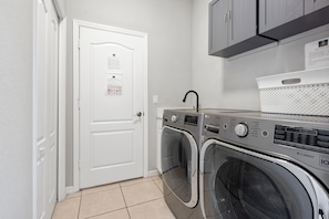A laundry room with two front-loading washing machines, a white door, and a notice on the wall. - The Triple Naples Collection - 3 Homes • Pools & Spas • King Beds! (Naples)