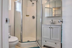 A bathroom with a glass-enclosed shower, a toilet, and a white cabinet with a mirror above it. - PB Chic Boho Studio w/ Parking (San Diego)