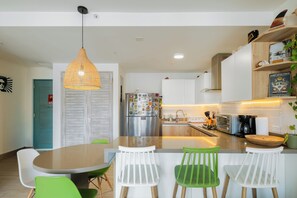 A modern kitchen with a central island, white bar stools, a hanging light fixture, and a refrigerator adorned with magnets. - El Patio Chame. Oceanfront Getaway. 2 bedrooms & 2 bathrooms. (Chame)