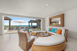 A spacious living area with a view of the sea, furnished with wicker sofas and a round coffee table. - Beautiful House at Coronado Quivira Golf Course (Cabo San Lucas)