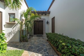 A stone pathway leading to a dark wooden door, flanked by greenery and a white building with a tiled roof. - Beautiful House at Coronado Quivira Golf Course (Cabo San Lucas)