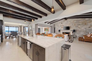 A modern kitchen with a central island, dark wooden beams, and a stone wall. - Beautiful House at Coronado Quivira Golf Course (Cabo San Lucas)