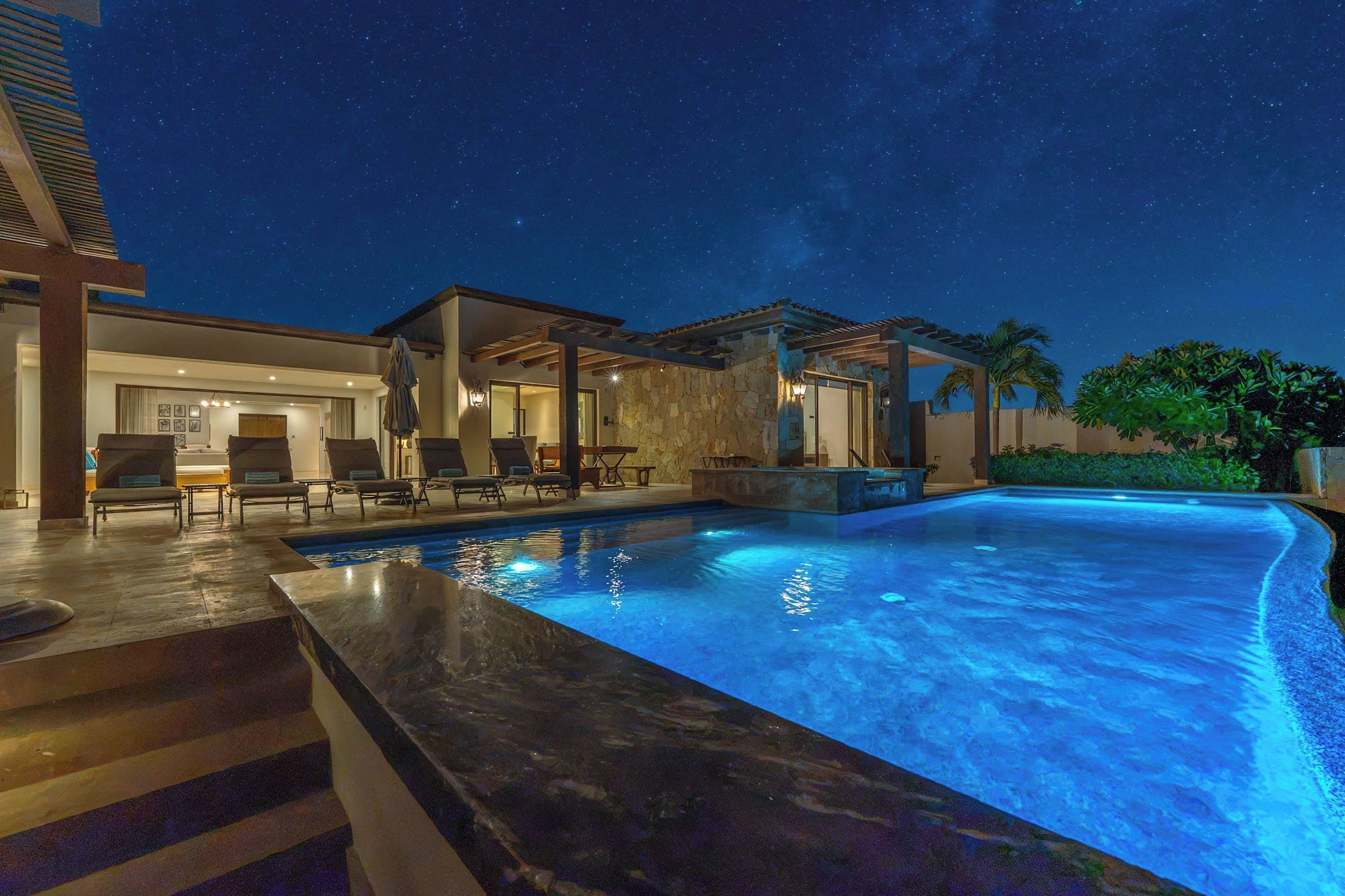 A swimming pool with a stone facade and a patio area with lounge chairs.