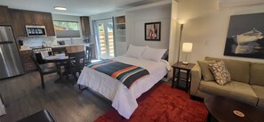 A compact hotel room with a kitchenette, a bed with a colorful blanket, a sofa, and a painting on the wall. - Entire guest suite in Northwest Bend just a few minutes walk from downtown (Bend)