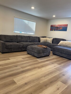 A modern living room with a sectional sofa, a matching ottoman, and a painting on the wall. - Surfcity Getaway 5min walk to beach and Main St (Huntington Beach)