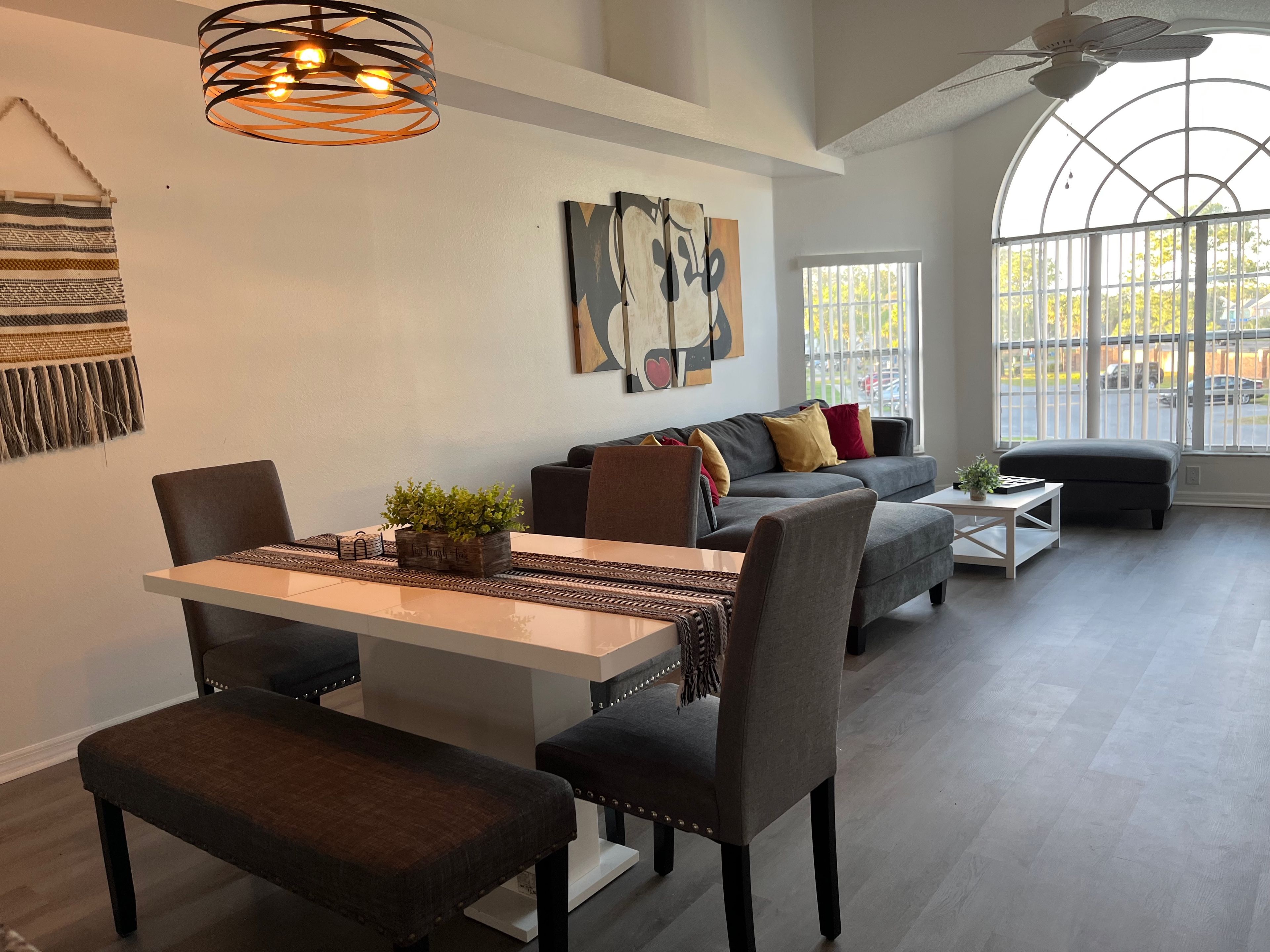 A modern living room with a dining area, a large window with a view, and a ceiling fan.