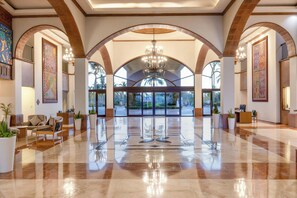 Eine großzügige Lobby mit hoher Decke, rundbogigen Durchgängen und einem zentralen Kronleuchter.