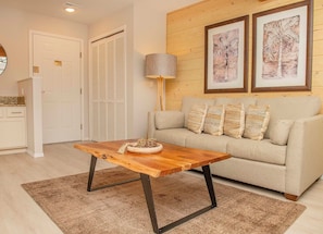 A living room with a wooden coffee table, a sofa with patterned cushions, a lamp, and two framed artworks on the wall. - Still Waters Resort 1BR Condo – Pools, Lake & Marina (Branson)
