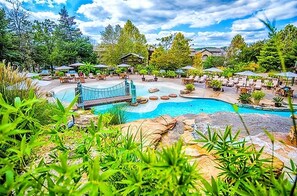 A pool area with lounge chairs and umbrellas, surrounded by greenery. - Still Waters Resort 1BR Condo – Pools, Lake & Marina (Branson)