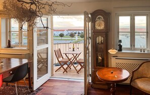 Quarto com mesa de madeira, uma cadeira, um relógio e vista para o exterior.
