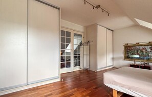 Ein Schlafzimmer mit Bett, Kleiderschrank, einer Tür mit Fensterglas und einem Bild an der Wand.