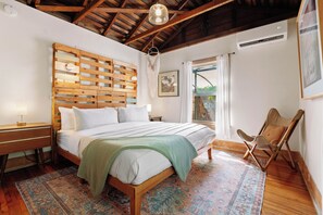 A bedroom with a wooden headboard, a bed with white linens, a nightstand with a lamp, a chair, and a patterned rug. - Venice Urban Farm 3BR Sauna RV & Chickens! (Los Angeles)