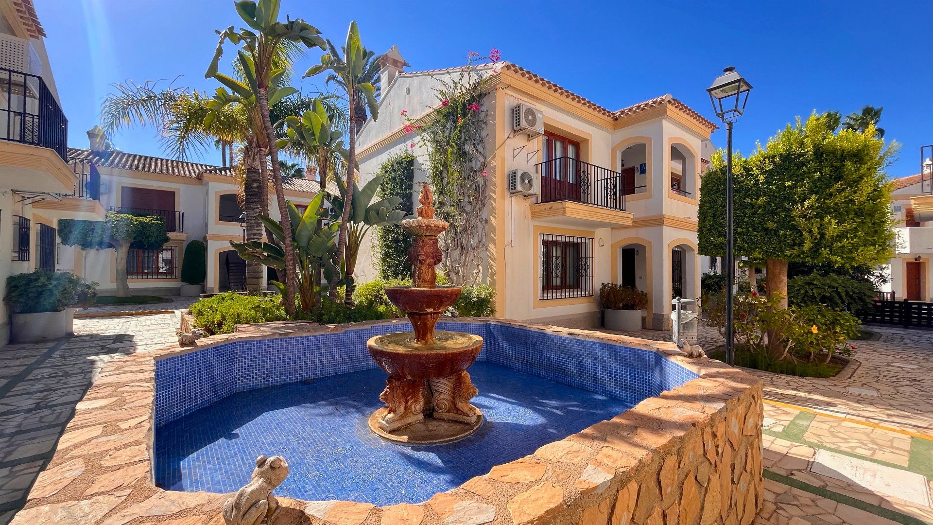 A courtyard with a fountain, palm trees, and a building with balconies.