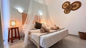 A bedroom with a canopy bed, two bedside lamps, a wooden nightstand, and a woven basket. - Bohemian-style flat with swimming pools, near the beach (Vera)