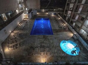 Ein Poolbereich auf dem Dach mit einem rechteckigen Pool und einem kleineren kreisförmigen Pool, umgeben von Liegestühlen und einer Treppe.