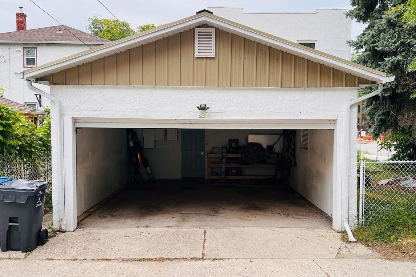 A garage with a white exterior and a brown roof, containing various tools and equipment.