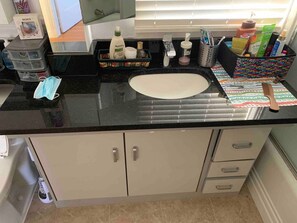Un baño con encimera negra, lavamanos y armarios para almacenamiento.