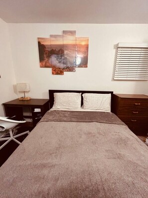 Una camera da letto con un letto, un comodino, una lampada, una cassettiera e un quadro appeso al muro.