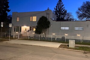 A two-story building with a fenced front yard, a visible entrance, and a street sign indicating parking restrictions.