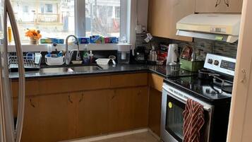 A compact kitchen with a stove, oven, and sink, wooden cabinets, and a window with blinds.