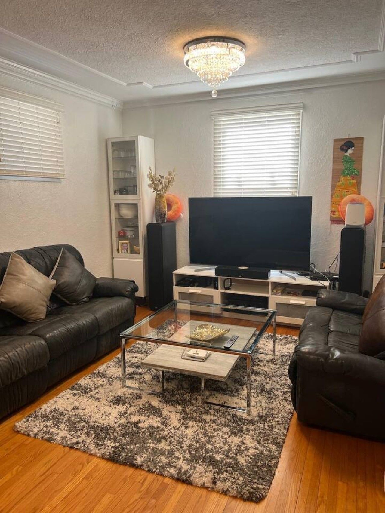 A living room with a black leather sofa, a glass coffee table, a flat-screen TV, and a chandelier.