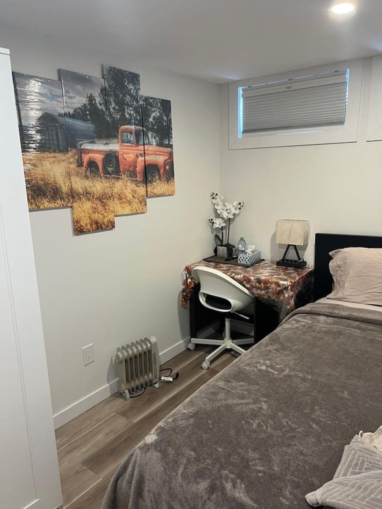 A bedroom with a bed, a desk with a chair, a radiator, and wall art.