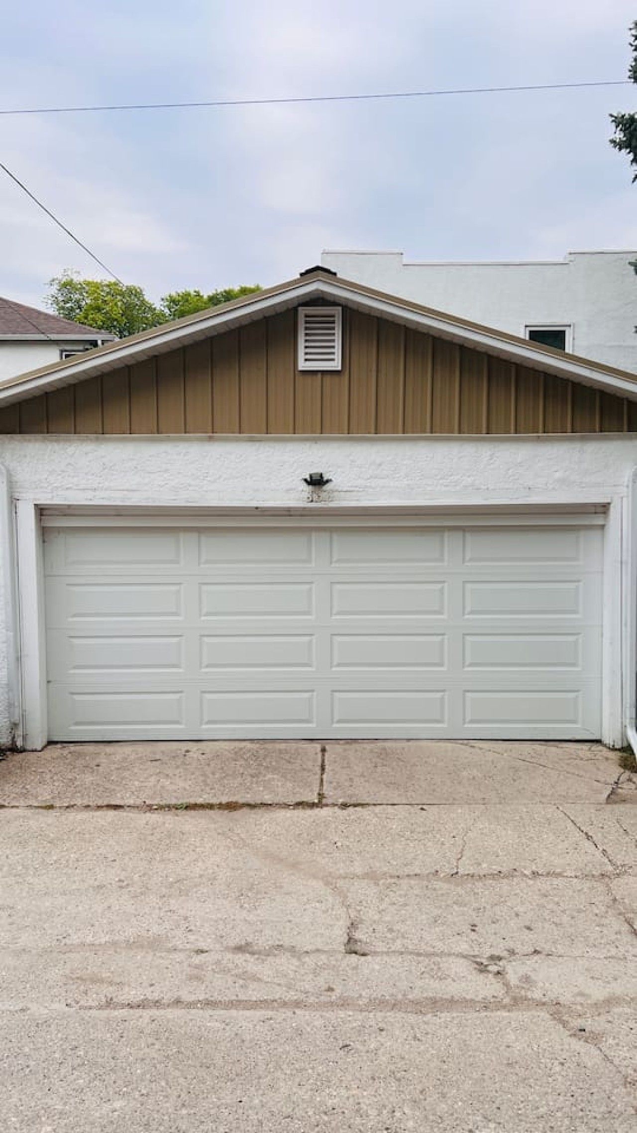 A garage with a white door, a brown roof, and a concrete driveway.