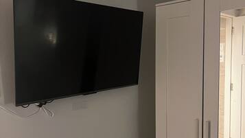 Une pièce avec un téléviseur à écran plat fixé au mur, une armoire blanche et une porte visible donnant sur une autre pièce.