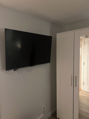 Ein Zimmer mit einem an der Wand befestigten Flachbildfernseher, einem weißen Kleiderschrank und einer sichtbaren Tür zu einem anderen Raum.