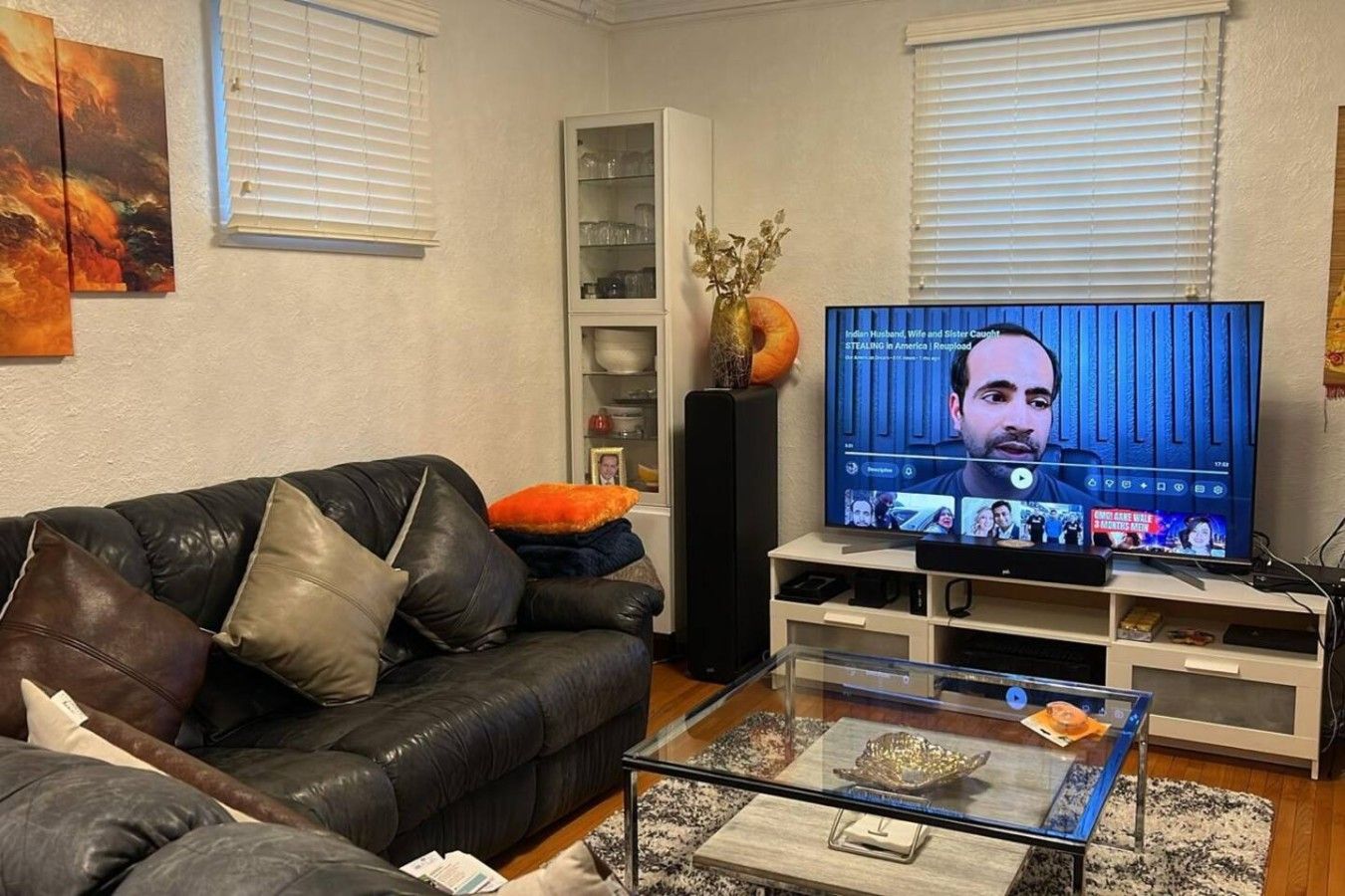 Un salon avec un canapé en cuir noir, une table basse en verre, un téléviseur à écran plat et un meuble de rangement blanc.