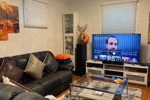 Ein Wohnzimmer mit einem schwarzen Ledersofa, einem Glastisch, einem Flachbildfernseher und einer weißen Unterhaltungsanlage.