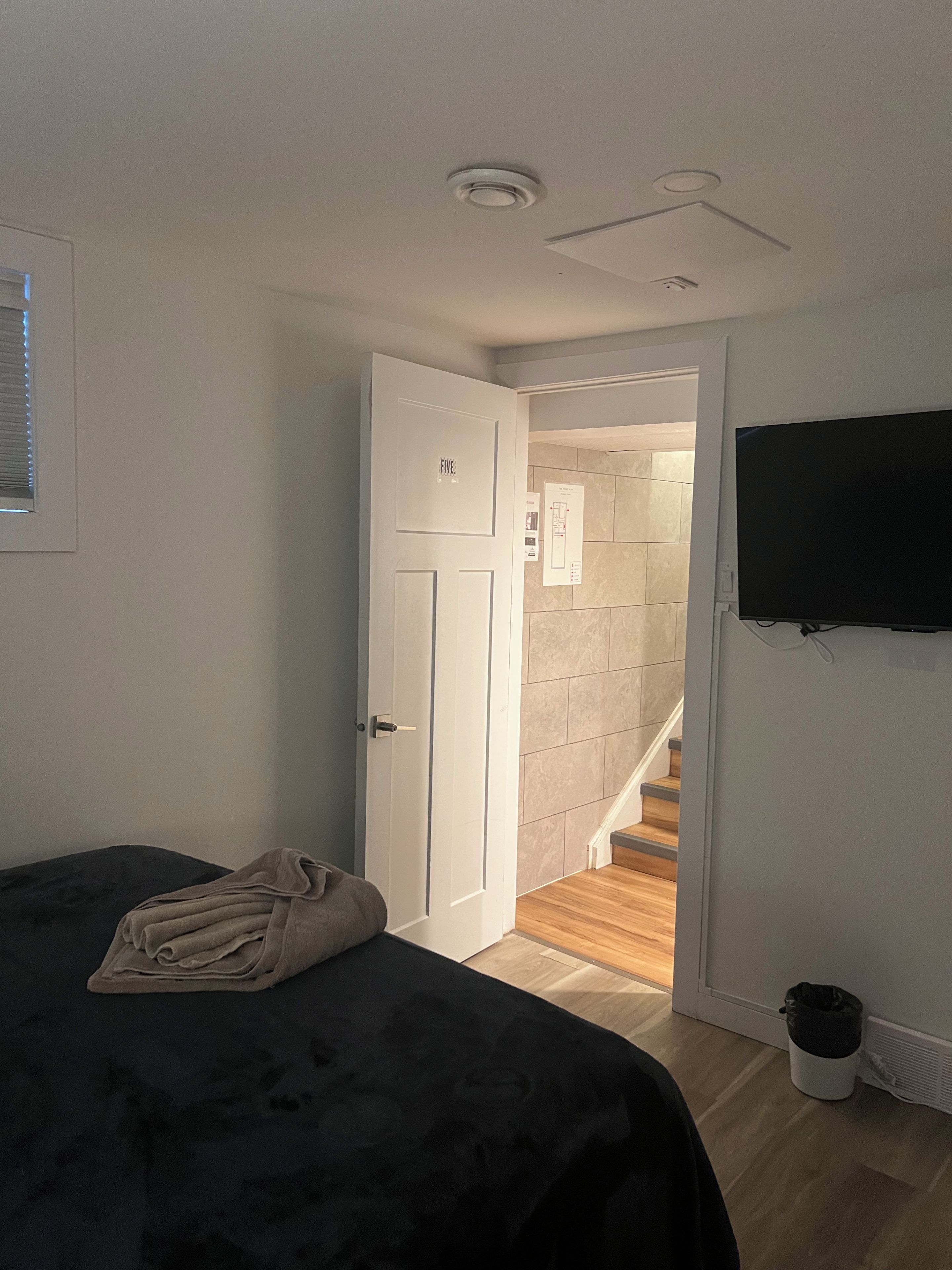 Une chambre à coucher avec un lit, une télévision, une porte et un escalier menant à une autre pièce.